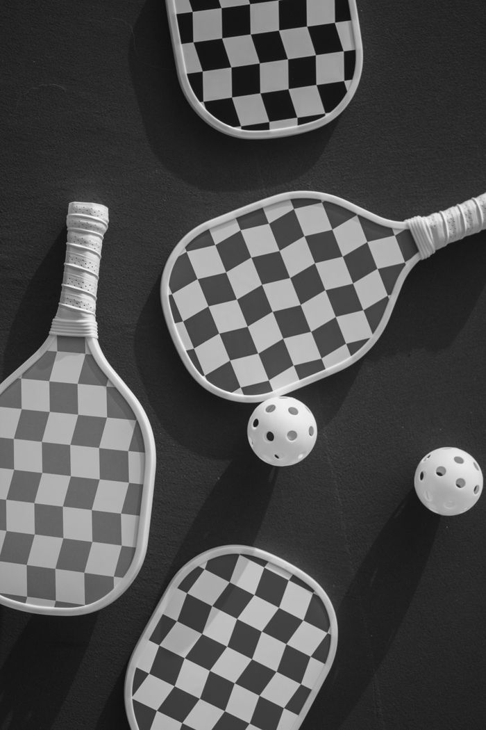 services-01 Checkered pickleball paddles and balls on a dark background, viewed from above.
