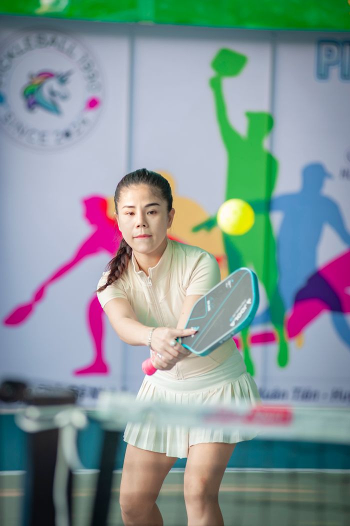 Focused Asian woman playing indoor pickleball with colorful background in Hanoi, Vietnam