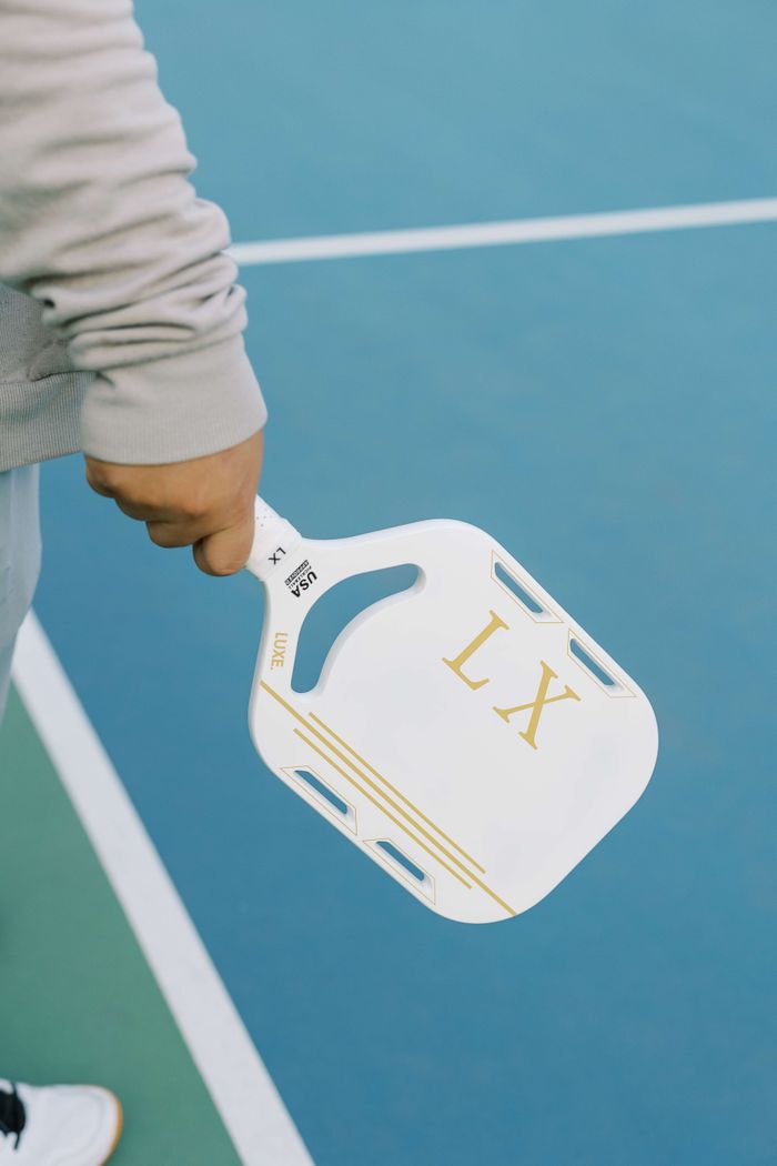 services-04 Close-up of hand holding a pickleball paddle on an outdoor court.