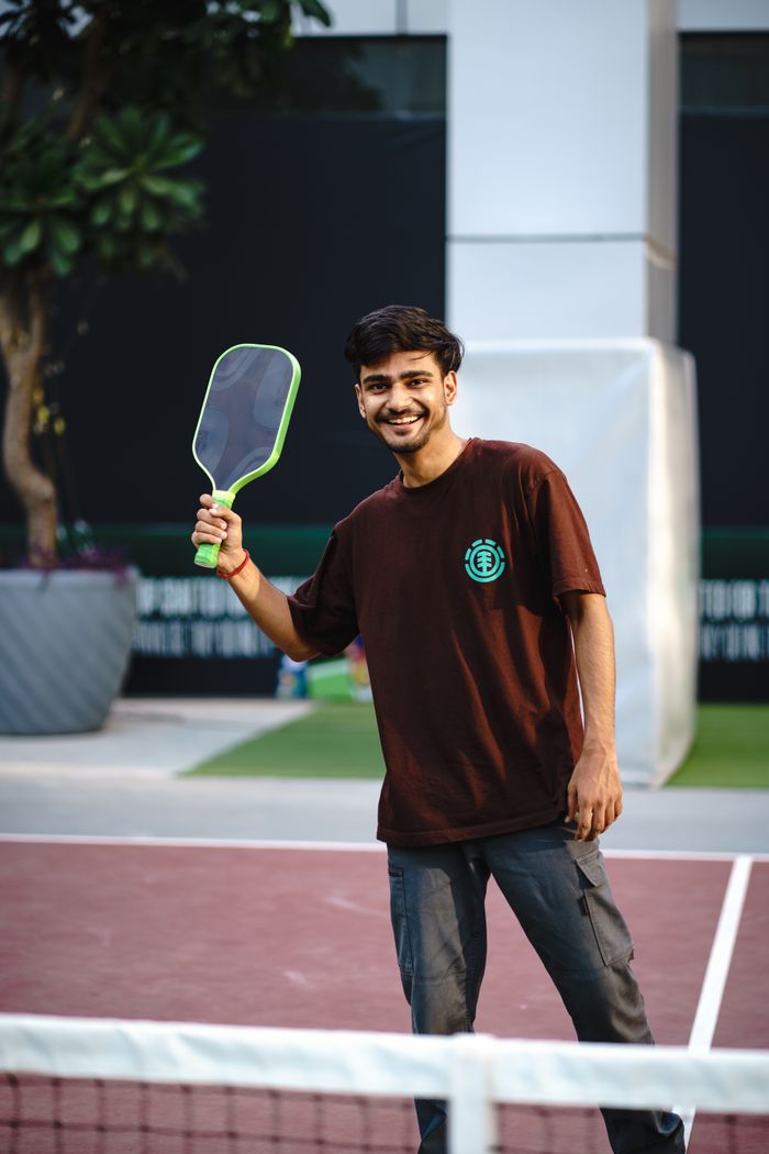 services-03 Smiling young man playing pickleball on an outdoor court, showcasing active lifestyle and sportsmanship.